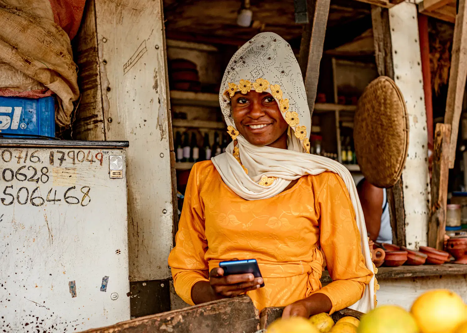 A fruit seller in Dar es Salaam smiling at her phone at her stall